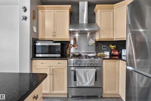 Stainless steel appliances, black tile backsplash, light wood cabinetry, black countertops, and a built-in microwave - 4471 Mccrae Avenue Nw, Edmonton, AB - Indoor Photo Showing Kitchen