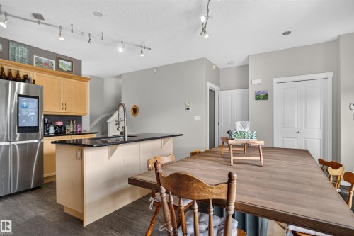 Kitchen island with dark countertop, stainless steel refrigerator, and wood-finish flooring - 4471 Mccrae Avenue Nw, Edmonton, AB - Indoor