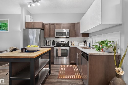 Contemporary kitchen featuring stainless steel appliances, wood-finish cabinetry, light-toned countertops, and a white subway tile backsplash - #34 6520 2 Av Sw, Edmonton, AB - Indoor Photo Showing Kitchen With Stainless Steel Kitchen With Upgraded Kitchen