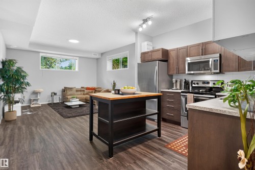 Modern kitchen featuring stainless steel appliances, wood-finish flooring, and light gray walls - #34 6520 2 Av Sw, Edmonton, AB - Indoor Photo Showing Kitchen With Stainless Steel Kitchen