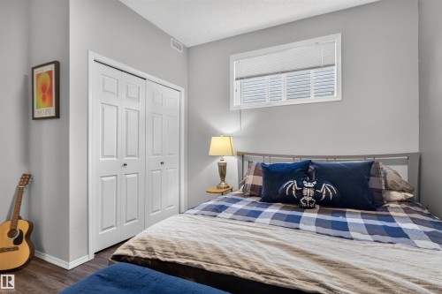 Wood-finish flooring, white bi-fold closet doors, neutral wall color, and a window with horizontal blinds - #34 6520 2 Av Sw, Edmonton, AB - Indoor Photo Showing Bedroom
