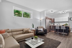 Open-concept living area with wood-finish flooring, a contemporary kitchen featuring stainless steel appliances, dark wood-finish cabinetry, and white overhead cabinetry - 