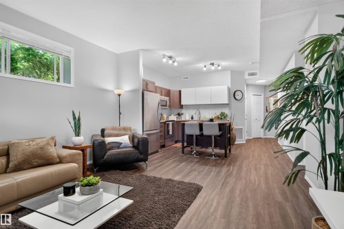 Open-concept living area featuring wood-finish flooring, recessed lighting, and a kitchen with stainless steel appliances - #34 6520 2 Av Sw, Edmonton, AB - Indoor Photo Showing Living Room