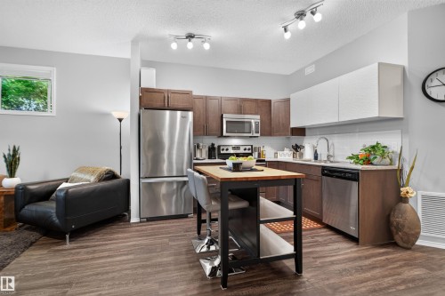 Open-concept living space with wood-finish flooring, stainless steel appliances, and track lighting - #34 6520 2 Av Sw, Edmonton, AB - Indoor Photo Showing Kitchen With Stainless Steel Kitchen