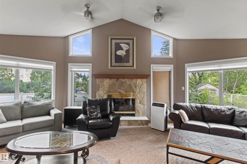 Vaulted ceiling with semi-flush mount light fixtures, stone-surround fireplace with hearth, and multiple windows - 11139 157 Avenue Nw, Edmonton, AB - Indoor Photo Showing Living Room With Fireplace
