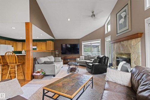 Vaulted ceiling with ceiling fan, stone-faced fireplace with wood mantel, wood-finish flooring, wood cabinetry, and large windows - 11139 157 Avenue Nw, Edmonton, AB - Indoor Photo Showing Living Room With Fireplace