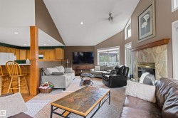 Vaulted ceiling with ceiling fan, stone-faced fireplace with wood mantel, wood-finish flooring, wood cabinetry, and large windows - 