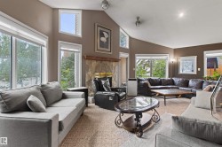 Vaulted ceiling living space featuring a stone-clad fireplace with a wood mantel, multiple windows, and recessed lighting - 