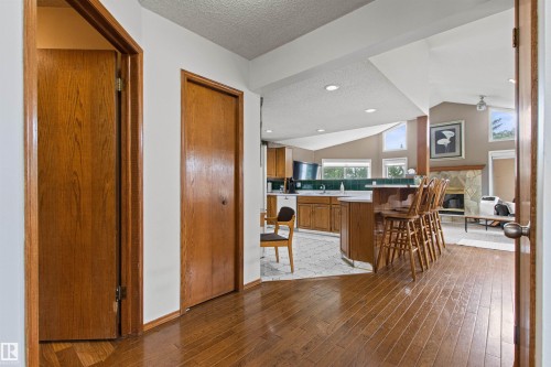Hardwood flooring throughout the entry, kitchen with wood cabinetry and a breakfast bar, and a stone fireplace with a wood mantle - 11139 157 Avenue Nw, Edmonton, AB - Indoor