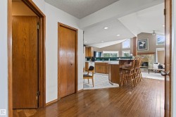Hardwood flooring throughout the entry, kitchen with wood cabinetry and a breakfast bar, and a stone fireplace with a wood mantle - 
