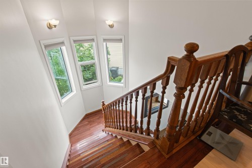 Hardwood staircase with turned balusters and newel posts, complemented by three window units with roller shades and two wall-mounted light fixtures - 11139 157 Avenue Nw, Edmonton, AB - Indoor Photo Showing Other Room