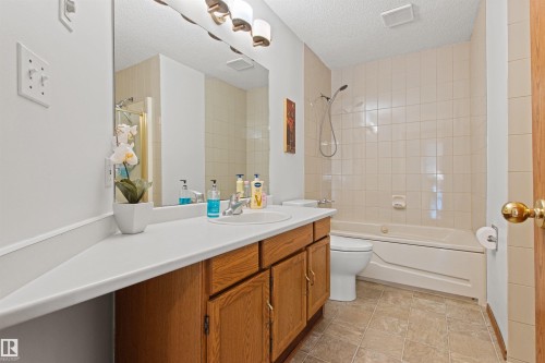 Bathroom featuring a wood-finish vanity with a white countertop, an integrated sink, a large wall-mounted mirror, and a tiled shower-over-tub combination - 11139 157 Avenue Nw, Edmonton, AB - Indoor Photo Showing Bathroom