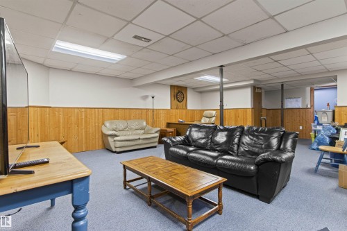 Expansive recreation room featuring wood paneling, drop ceiling with fluorescent lighting, and a partial wall separating spaces - 11139 157 Avenue Nw, Edmonton, AB - Indoor Photo Showing Basement