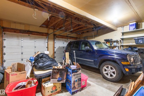 Two overhead garage doors, exposed wood beam ceiling, concrete flooring, and wall-mounted shelving - 11139 157 Avenue Nw, Edmonton, AB - Indoor Photo Showing Garage