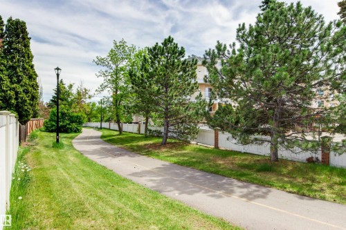 Paved pathway bordered by manicured lawn, established trees, and a white fence with brick pillars - 11139 157 Avenue Nw, Edmonton, AB - Outdoor