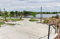 Concrete pathways and steps with black handrails, green spaces with mature trees, and a visible body of water - 
