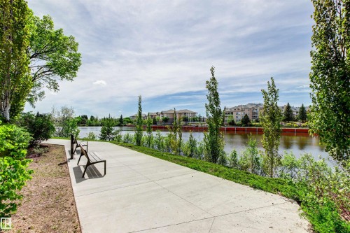 Paved pathway with two public benches, bordering a body of water, with distant buildings and lush trees - 11139 157 Avenue Nw, Edmonton, AB - Outdoor With Body Of Water With View