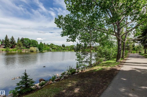 Paved pathway bordered by mature trees and lush greenery, alongside a tranquil body of water - 11139 157 Avenue Nw, Edmonton, AB - Outdoor With Body Of Water With View