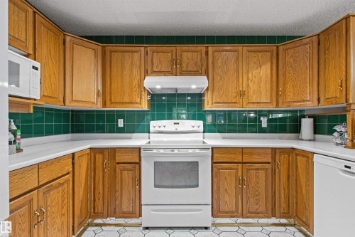 U-shaped kitchen featuring wood cabinetry, white countertops, green subway tile backsplash, and white appliances - 11139 157 Avenue Nw, Edmonton, AB - Indoor Photo Showing Kitchen