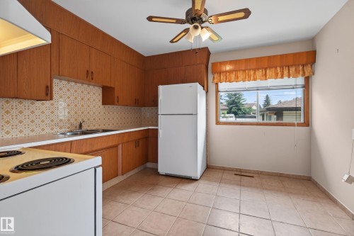 Kitchen featuring wood-finish cabinetry, tile backsplash, laminate countertops, and tile flooring - 8411 136 Avenue Nw, Edmonton, AB - Indoor Photo Showing Kitchen With Double Sink