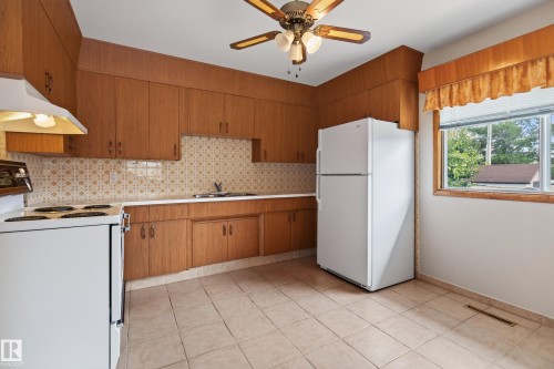Kitchen featuring extensive wood-finish cabinetry, white countertop, tile flooring, and a ceiling fan with integrated lighting - 8411 136 Avenue Nw, Edmonton, AB - Indoor Photo Showing Kitchen With Double Sink