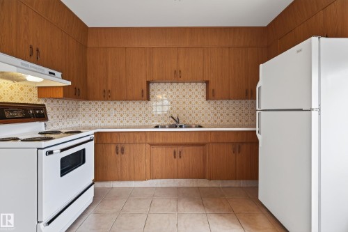 Kitchen featuring wood-finish cabinetry, tile flooring, and a patterned backsplash - 8411 136 Avenue Nw, Edmonton, AB - Indoor Photo Showing Kitchen With Double Sink