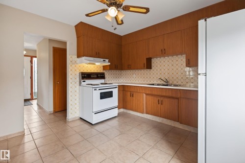 Tile flooring, wood-finish cabinetry, white appliances, patterned tile backsplash, and a ceiling fan with integrated lighting - 8411 136 Avenue Nw, Edmonton, AB - Indoor Photo Showing Kitchen With Double Sink