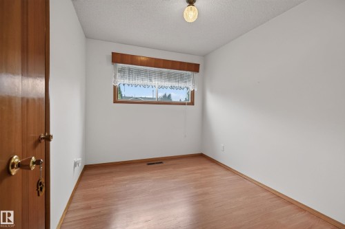 Wood-finish flooring, white painted walls, wood-framed window, wooden door with brass hardware, and a ceiling-mounted light fixture - 8411 136 Avenue Nw, Edmonton, AB - Indoor Photo Showing Other Room