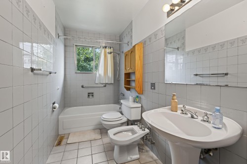 Pedestal sink, wall-mounted mirror, light fixture, built-in tub with shower, and tiled flooring - 8411 136 Avenue Nw, Edmonton, AB - Indoor Photo Showing Bathroom