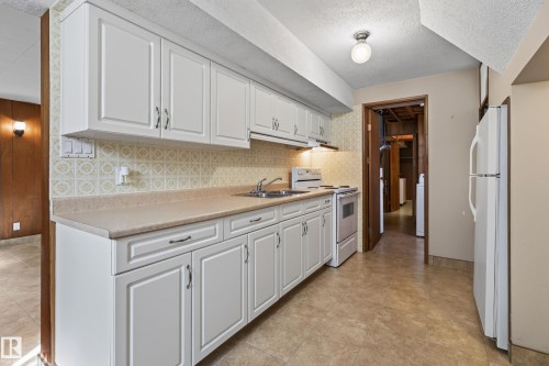 White cabinetry with dark hardware, a double basin sink, and a white electric range - 8411 136 Avenue Nw, Edmonton, AB - Indoor Photo Showing Kitchen With Double Sink