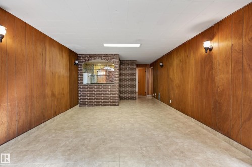 Spacious basement featuring warm wood-finish paneling throughout, polished concrete flooring, recessed ceiling lighting, and brick accent wall detail - 8411 136 Avenue Nw, Edmonton, AB - Indoor Photo Showing Other Room