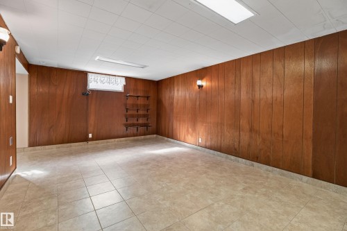 Wood paneling on walls, ceramic tile flooring, built-in shelving, two wall sconces, and overhead lighting - 8411 136 Avenue Nw, Edmonton, AB - Indoor Photo Showing Basement
