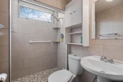 Pedestal sink with chrome fixtures, tiled shower with integrated shelving, and a wall-mounted storage cabinet - 8411 136 Avenue Nw, Edmonton, AB - Indoor Photo Showing Bathroom
