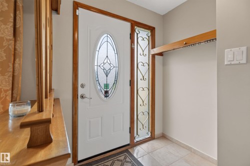Entryway featuring a white paneled door with an oval stained-glass insert, a sidelight with decorative metalwork, and tiled flooring - 8411 136 Avenue Nw, Edmonton, AB - Indoor Photo Showing Other Room