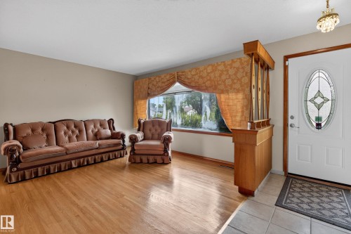 Wood-finish flooring, light tan wall color, built-in wooden room divider, white entry door with oval decorative glass, tiled entry floor - 8411 136 Avenue Nw, Edmonton, AB - Indoor Photo Showing Living Room