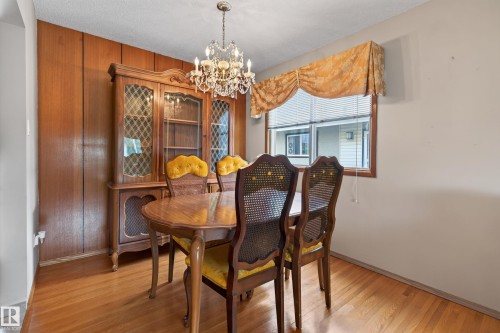 Wood-finish flooring, wood-paneled accent wall, and a crystal chandelier - 8411 136 Avenue Nw, Edmonton, AB - Indoor Photo Showing Dining Room