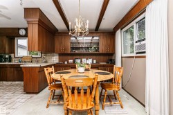 Dining area featuring a brass chandelier, wood-finish ceiling beams, and a window with white drapes - 