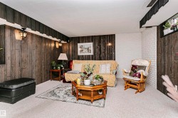 Carpeted room featuring wood-finish paneling and a white painted brick accent wall - 