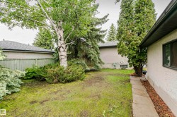 Private backyard space featuring mature trees, established shrubbery, a concrete paver walkway, wood fencing, and a stucco exterior - 