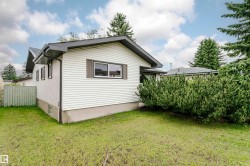 Exterior featuring white siding, a dark roofline, mature evergreen landscaping, and a grassy yard - 