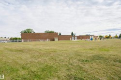 Expansive green space featuring a brick structure, a parking area, mature trees, and a visible playground apparatus - 