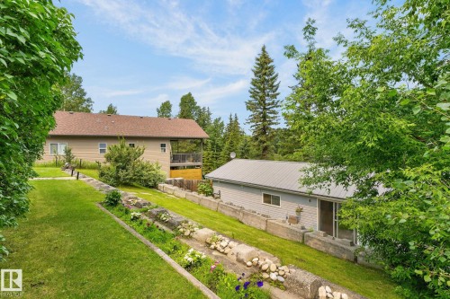 Sloping grassy yard with retaining walls, mature trees, and a two-story residence featuring a covered deck - 351 Smith Crescent, Rural Parkland County, AB - Outdoor