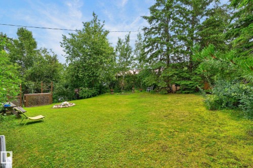 Expansive green lawn with mature trees, a built-in fire pit, and a wooden deck - 351 Smith Crescent, Rural Parkland County, AB - Outdoor