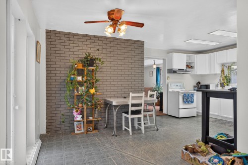 White upper and lower cabinetry, ceiling fan with integrated lighting, brick-pattern accent wall, and tiled flooring - 351 Smith Crescent, Rural Parkland County, AB - Indoor Photo Showing Kitchen