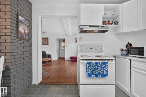White kitchen cabinetry, built-in range hood, and a white electric range, complemented by a gray brick wall feature and wood-finish flooring in the background - 351 Smith Crescent, Rural Parkland County, AB - Indoor
