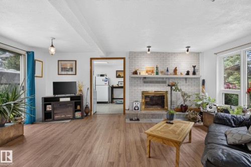 Wood-finish flooring, white brick fireplace with brass firebox, large window, and overhead lighting - 351 Smith Crescent, Rural Parkland County, AB - Indoor Photo Showing Living Room With Fireplace