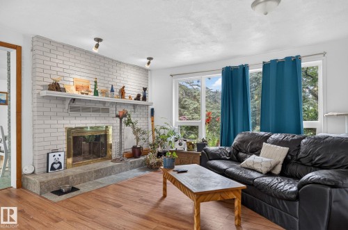 Living area featuring wood-finish flooring, a white brick fireplace with a stone hearth and mantel, and large windows - 351 Smith Crescent, Rural Parkland County, AB - Indoor Photo Showing Living Room With Fireplace
