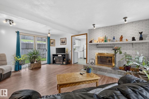 Wood-finish flooring, white painted brick fireplace with a gold-tone insert, stone hearth, and white mantel shelf - 351 Smith Crescent, Rural Parkland County, AB - Indoor Photo Showing Living Room With Fireplace