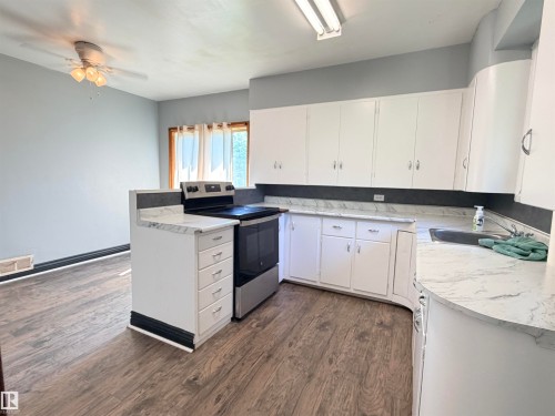 Wood-finish flooring, white cabinetry, integrated sink, and stainless steel range - 10416 100 Avenue, Westlock, AB - Indoor Photo Showing Kitchen