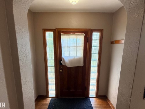Wood-finish flooring with a dark area rug, featuring a solid wood door flanked by glass block sidelights - 10416 100 Avenue, Westlock, AB - Indoor Photo Showing Other Room